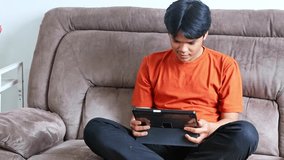 Young asian man joyfully using tablet computer on comfortable couch - Powered by Shutterstock - Get 15% off with code: PIKWIZARD15