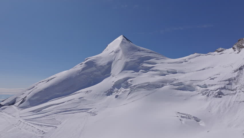 A powerful drone shot revealing massive overhanging seracs and towering ice cliffs in Saas-Fee, Switzerland. The frozen formations glisten under alpine light, showcasing the raw power of the glacier.
