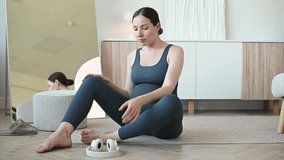 Expecting mother in sportswear sitting on the floor and putting on headphones before starting a prenatal meditation session. Calm pregnancy, relaxation and self care concept. - Powered by Shutterstock - Get 15% off with code: PIKWIZARD15