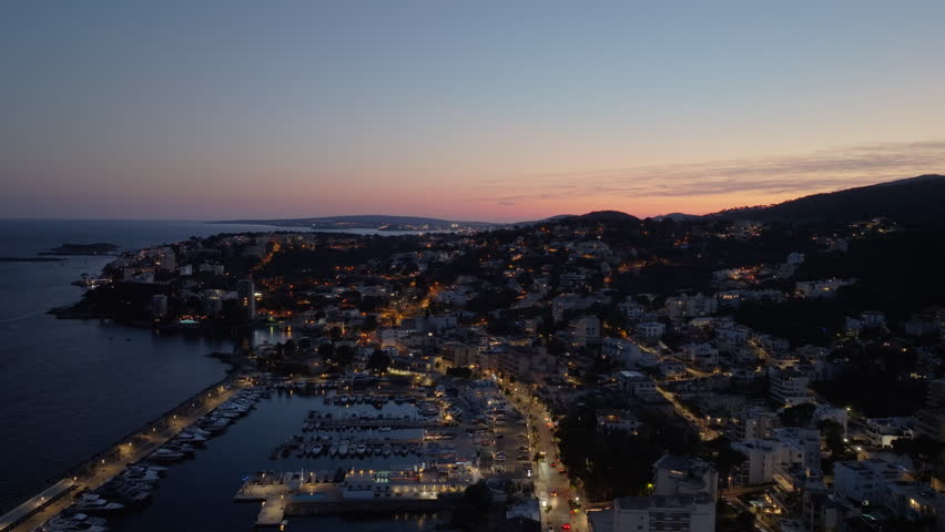 Aerial perspective of Cala Major marina in Mallorca, Spain. City lights illuminating the coastline as twilight descends over Mediterranean Sea