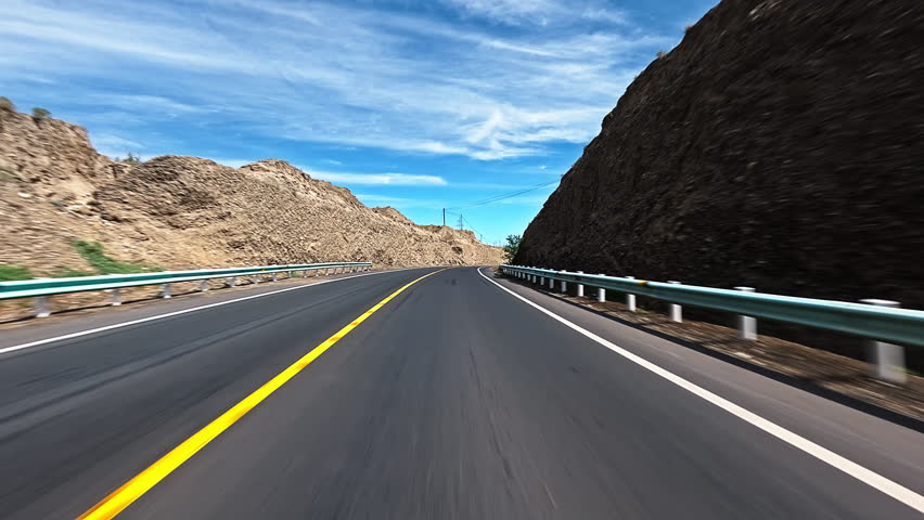 Driving car on an empty asphalt highway through a rocky mountain landscape under blue sky