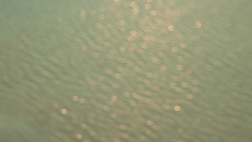 Abstract scene of warm sunlight bokeh and shimmering reflections on blurred water surface, minimal and dreamy summer texture.