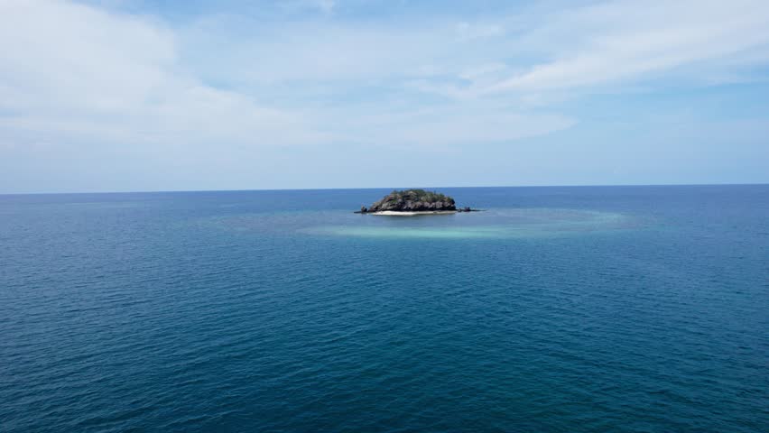 Aerial drone footage of a small, remote rocky island (islet) in the middle of a vast blue ocean. Concept of isolation, solitude, or escape. Indonesia.
