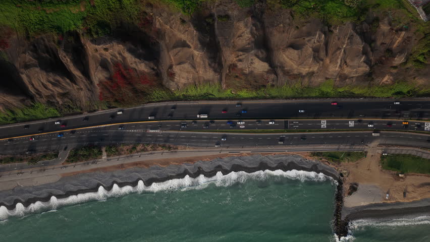 Aerial view capturing cars driving on Circuito de Playas highway along Costa Verde with waves crashing on the shoreline in Lima