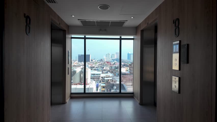 Building corridor with two elevators facing a window showing urban skyline buildings