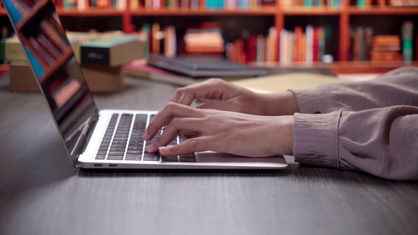 Close Up of Student Hands Typing Rapidly on Laptop Keyboard in a University Library