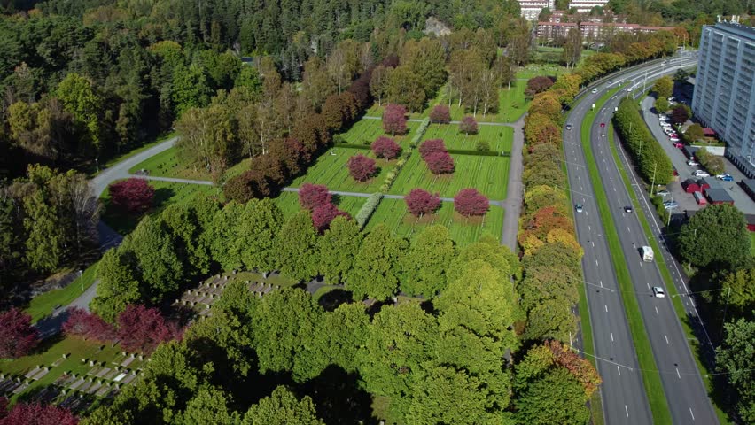 High angle aerial view of Kviberg Cemetery with red leaved trees, grave plots, and multi-lane road in Gothenburg, Sweden