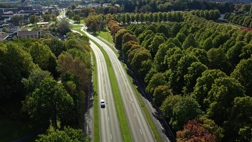 Smooth tilt up drone view of Kortedalavägen road curving through town and green trees near Kviberg Cemetery in Gothenburg, Sweden