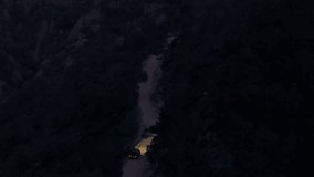 Stunning aerial footage of car with headlights on, driving along remote, winding dirt road through a dark mountain forest at dusk - Powered by Shutterstock - Get 15% off with code: PIKWIZARD15