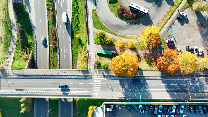Drone shot over road interchange with vehicles and bright autumn trees in morning light.