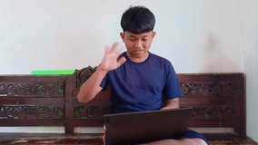 An Indonesian youth is having a cheerful video conference using a laptop, happily waving hello to the camera. Perfect for themes of remote work, online learning, and technology. - Powered by Shutterstock - Get 15% off with code: PIKWIZARD15