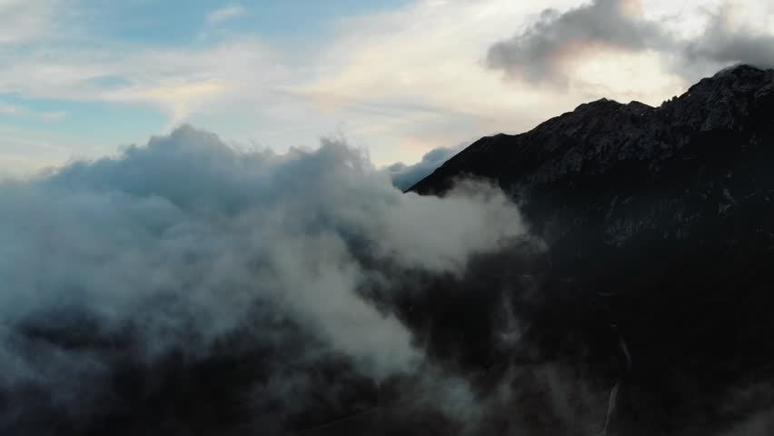Aerial drone view of mist and clouds drifting around rugged Sierra Nevada peaks with dramatic light and dark mountain slopes creating powerful and mysterious high altitude scenery