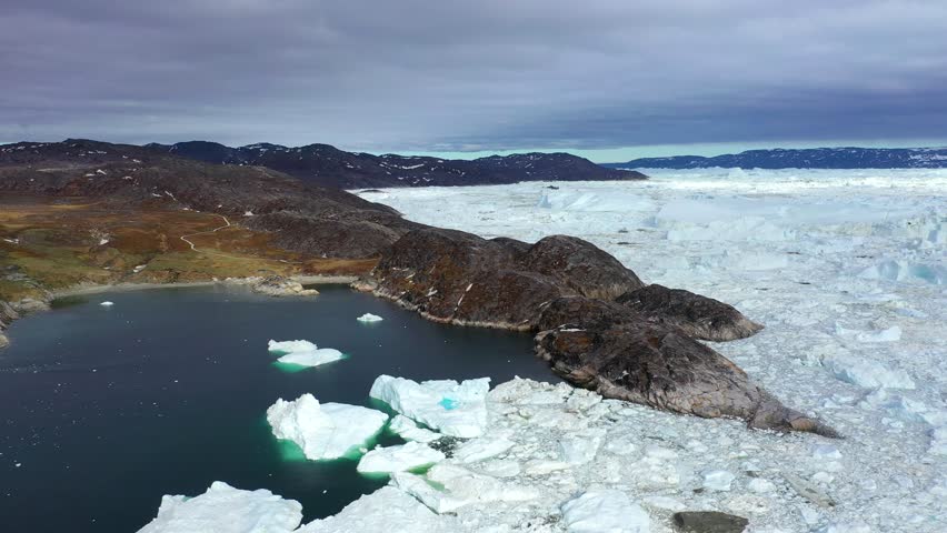 Beautiful icebergs float in calm waters, reflecting the surrounding mountains. This serene landscape captures the beauty of nature in Greenland on a sunny day, showcasing its unique features.