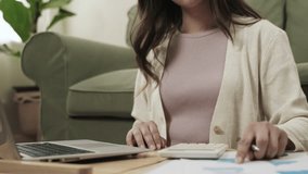 Selection focuses on the hand. Close up of young woman sitting and using a calculator for analyzing financial data together with a laptop computer about her family business in living room at her home. - Powered by Shutterstock - Get 15% off with code: PIKWIZARD15
