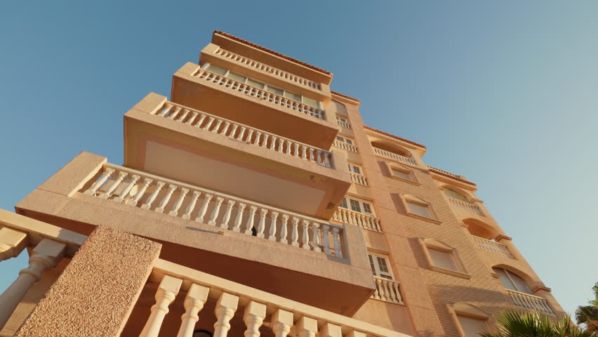 Hotel building with corner balconies under blue sky in urban cityscape low angle shot. Residential real estate attracts tourists to town. City architecture