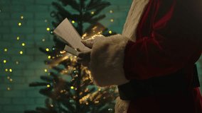 Santa Claus reads a wish list in front of a beautifully lit Christmas tree, capturing festive holiday spirit. - Powered by Shutterstock - Get 15% off with code: PIKWIZARD15