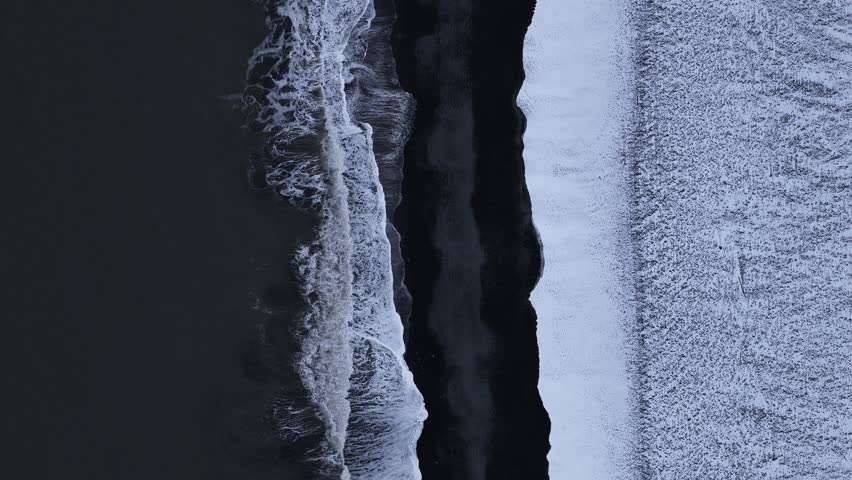 Aerial view of the dramatic contrast between the dark black sand beach and the frothy white waves crashing along the shore, Iceland, Iceland.