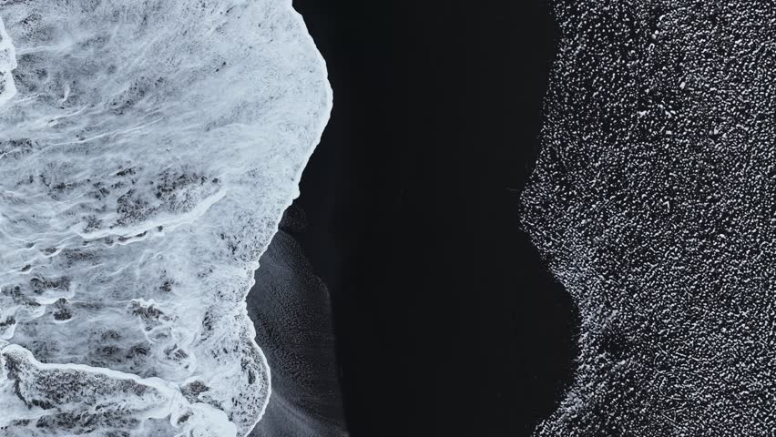 Aerial view of the stark contrast between the jet-black volcanic sand and the frothy white waves crashing along the shore, Iceland, Iceland.