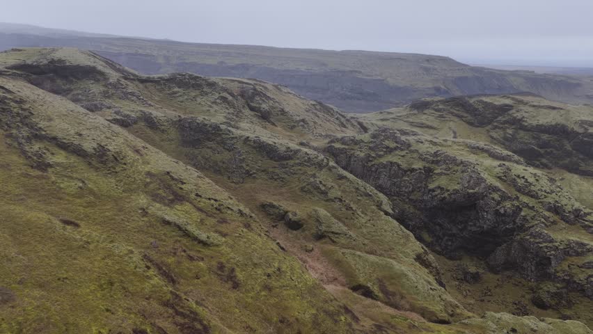 Aerial view of a stark white glacier snaking between dark hills and vibrant green valleys, creating a beautiful contrast in Iceland