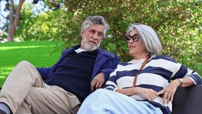Lovely senior couple with gray hair sitting on a park bench and talking. Relaxed retired man and woman enjoying a sunny day outdoors - Powered by Shutterstock - Get 15% off with code: PIKWIZARD15