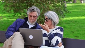 Elderly man and woman sitting on a park bench looking at a laptop with worried and shocked expressions, displaying concern over what they see - Powered by Shutterstock - Get 15% off with code: PIKWIZARD15