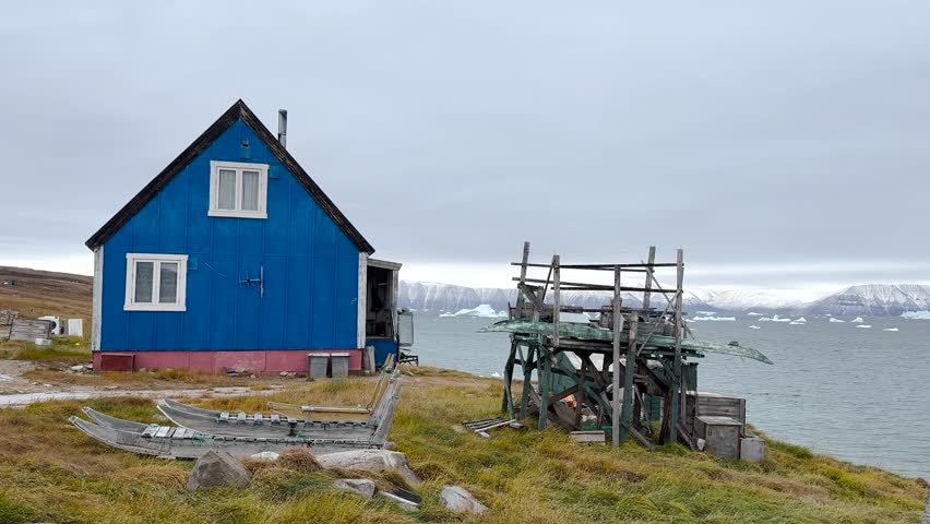Brightly colored houses stand near the ocean, surrounded by icebergs. The cloudy sky adds a unique ambiance to this tranquil Greenlandic landscape. Nature and culture blend beautifully here.