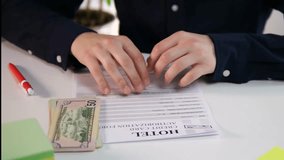 A close up shot of a businessmans hands filling out a hotel registration form, with cash placed nearby on the table. The action of his finger tracing the data fields illustrates careful review and the - Powered by Shutterstock - Get 15% off with code: PIKWIZARD15