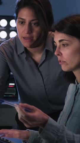 Professional women discussing a project on a laptop in a data center or control room at night