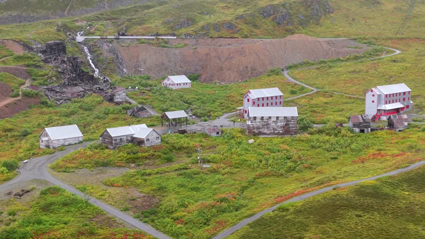 Aerial view of buildings with red roofs surrounded by lush green grass and a waterfall cascading down a rocky cliff, Palmer, Alaska, United States.