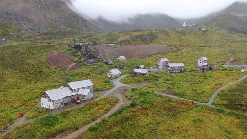 Aerial view of buildings scattered across the landscape, nestled beneath misty mountains, showcasing muted greens and browns, Palmer, Alaska, United States.