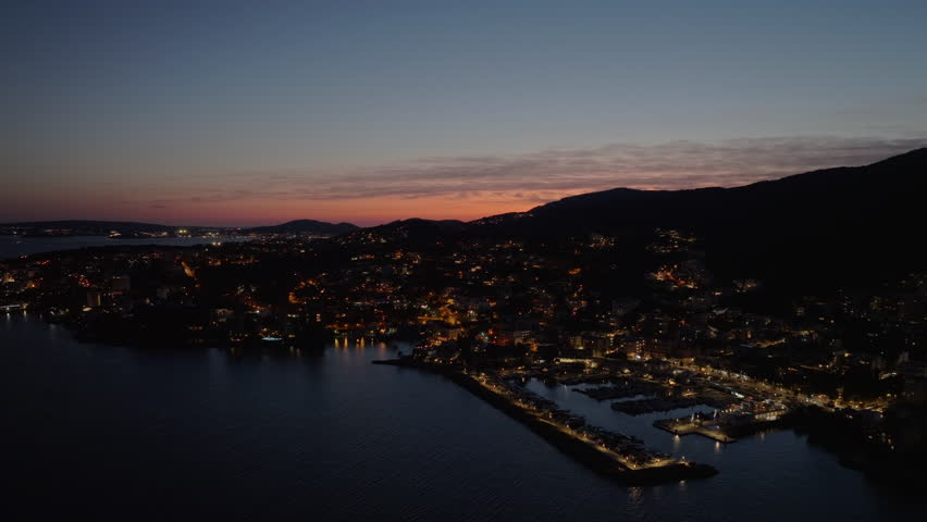 Aerial footage showing illuminated cityscape of a coastal town in Palma de Mallorca, Spain, with a beautiful sunset sky