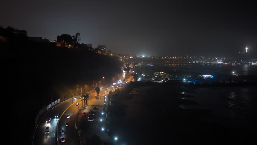 Aerial night view of Circuito de Playas highway in Lima, Peru. Illuminated traffic flowing along the dark coast of Pacific Ocean