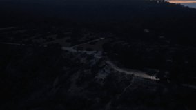 Tripod shot from high-altitude perspective of lone SUV driving on a winding, unpaved road through a dark, rugged landscape during twilight hour - Powered by Shutterstock - Get 15% off with code: PIKWIZARD15