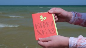 Woman at the Beach Holds Up a Handmade Red Merry Xmas Card with Holly and Berries in front of the Lake 4K Video Stock Footage - Powered by Shutterstock - Get 15% off with code: PIKWIZARD15