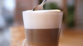 Close up of a silver spoon stirring a freshly made latte macchiato in a clear glass cup, mixing the distinct layers of espresso, steamed milk, and creamy foam on a coffee shop table - Powered by Shutterstock - Get 15% off with code: PIKWIZARD15