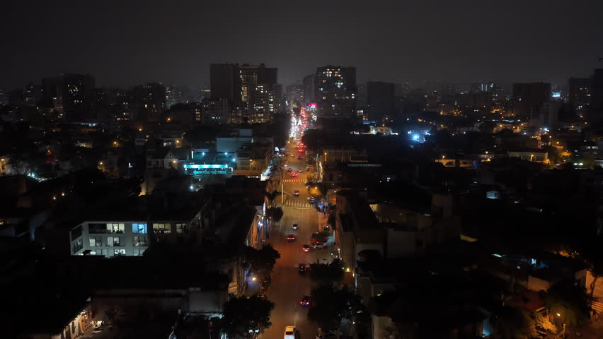 Aerial night view of Lima, Peru flying towards the city center with car traffic moving on the street. Cityscape with illuminated buildings