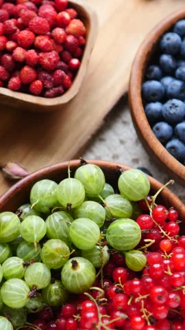 Freshly picked summer berries, including wild strawberries, blueberries, gooseberries, and red currants, served in wooden bowls for a healthy, natural, and antioxidant rich vegan dessert