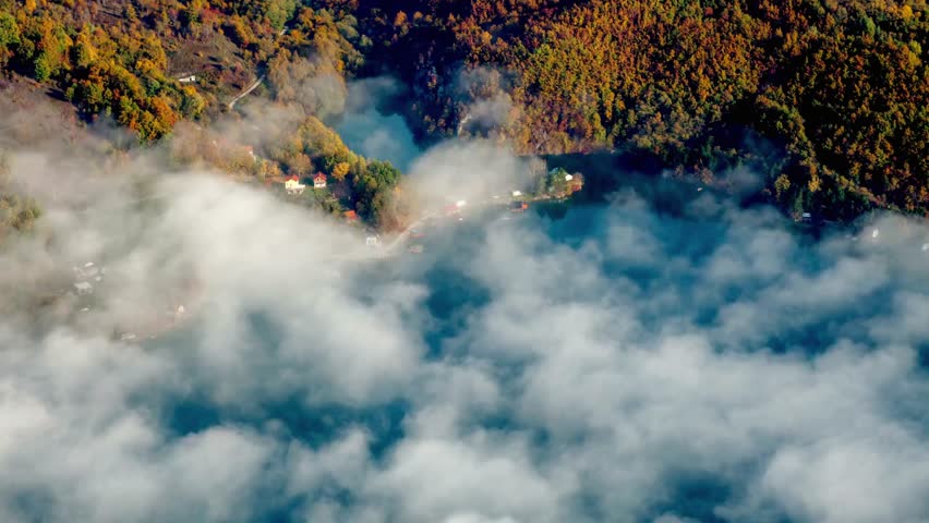 Aerial view of a serene lake surrounded by colorful autumn trees and low clouds
