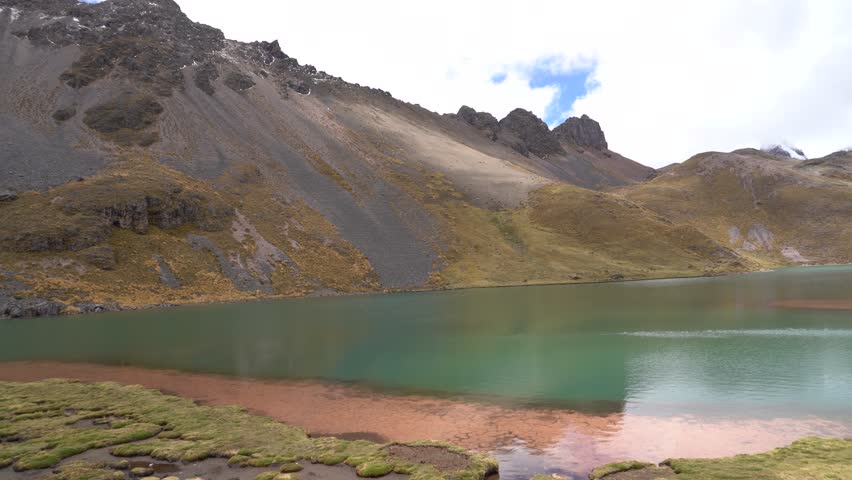 A smooth panning shot across one of the Seven Glacial Lakes of Ausangate, showcasing its stunning blue and green waters with multiple mountain peaks visible along the sweep