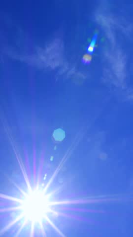 Bright sunlight streaming through a clear blue sky, creating a beautiful starburst effect and colorful lens flare. Warm sunbeams radiate across the serene atmosphere on a perfect summer day
