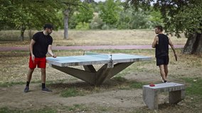 Friends enjoy a fun game of table tennis on an outdoor concrete table in a lush green park. They laugh and play, engaging in a recreational activity on a pleasant day. - Powered by Shutterstock - Get 15% off with code: PIKWIZARD15