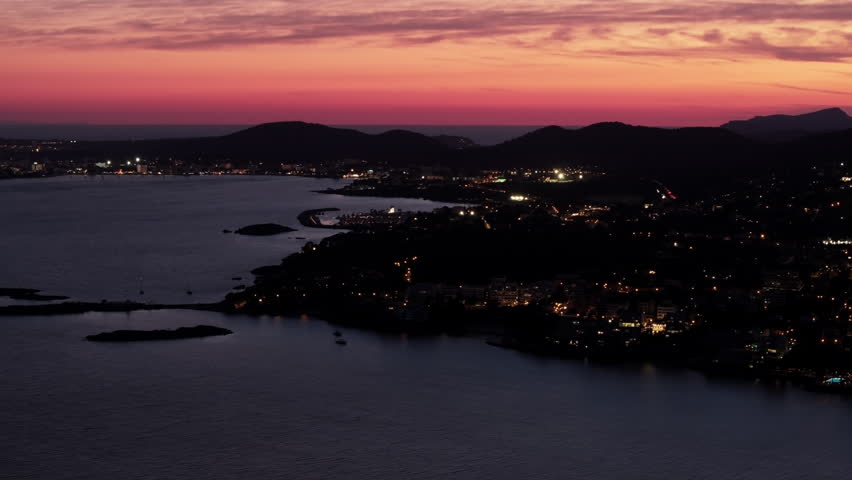 Aerial view showing the illuminated coastline of Mallorca in Spain during a colorful sunset. Scenic view of the sea and mountains at dusk