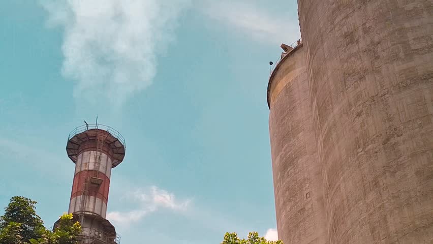 Tall factory chimney emitting thick white smoke into the blue sky, symbolizing air pollution.