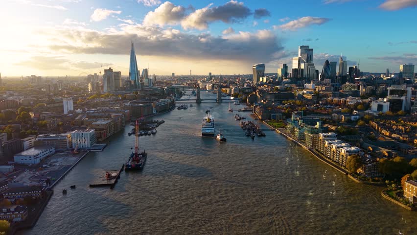 Panoramic aerial view of the skyline of London, United Kingdom, along the Thames river with boat traffic and Tower Bridge during golden sunset time