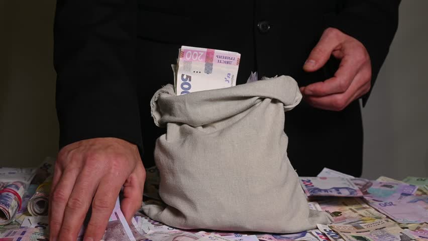Person putting Ukrainian hryvnia into canvas bag symbolizing savings, profit, and secure money storage. Hands filling sack with paper money representing wealth, financial safety, and capital growth.