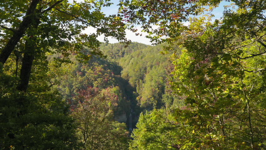 A view through lush autumn foliage of mountains and a waterfall. Autumn landscape.