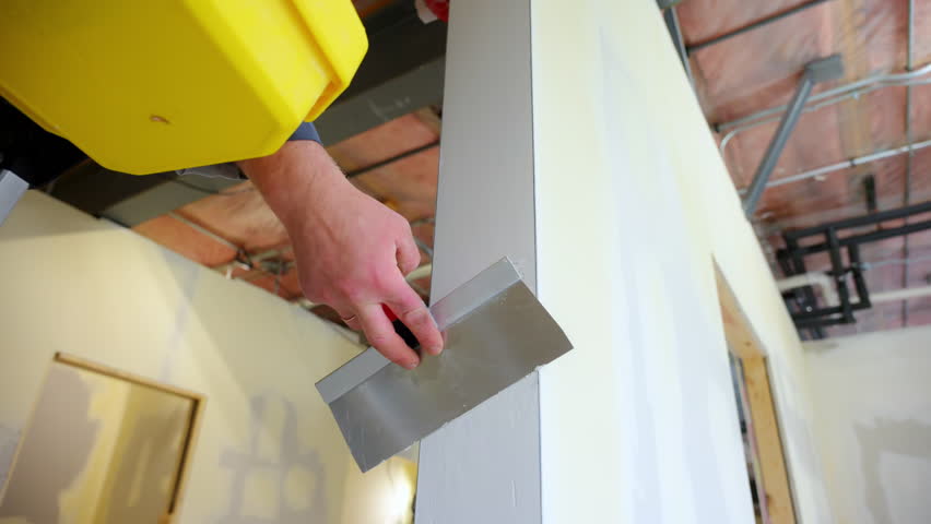 construction worker applies joint compound to drywall end using a metal spatulas. Worker smoothing seams and preparing the surface for finishing