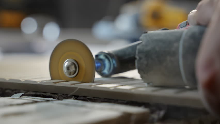 Worker is cutting ceramic tile with an small electric angle grinder. Workshop or renovation site, focusing on craftsmanship, precision, and manual labor.