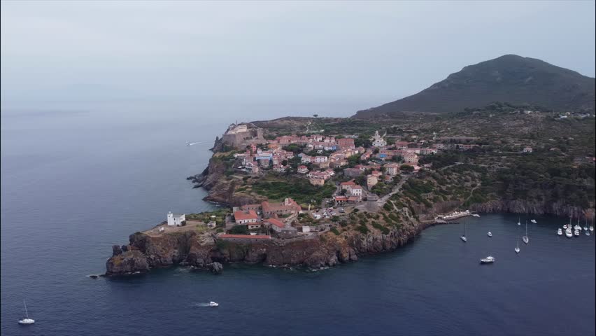 Aerial view of the historic town of Capraia Isola, Livorno, Tuscany, Italy. Colorful houses on a rocky cliff surrounded by the Mediterranean Sea.