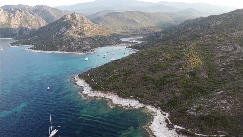 Aerial view of Plage de Fiume Santu beach, Corsica, France. Turquoise waters and boats anchored in a scenic wild bay surrounded by rocky hills.
